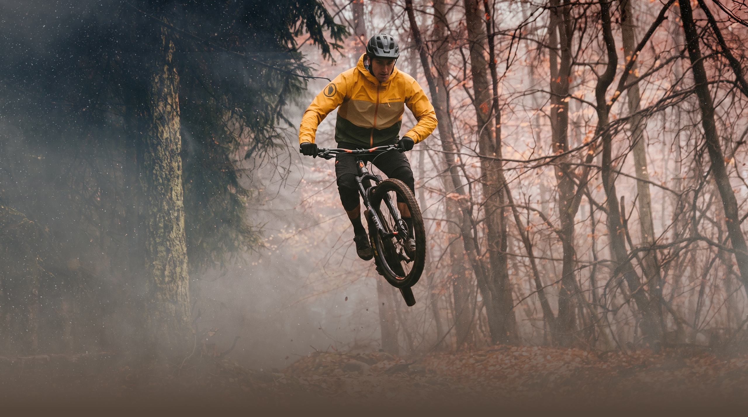 Rider in a SingleTrack jacket launching off a jump through a misty autumn forest